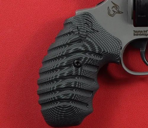 Detailed view of the engraved black grip on a Taurus Defender 856 revolver against a red background.