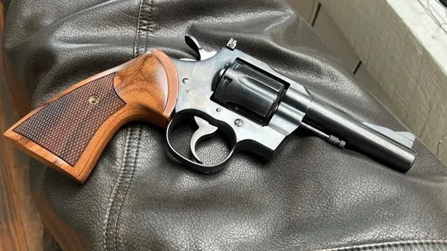 Colt Trooper MK III revolver with wooden grips, resting on a black leather surface.
