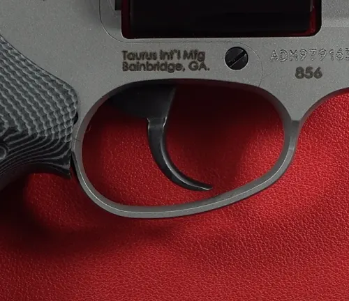Trigger and trigger guard of a Taurus Defender 856 revolver on a red background.