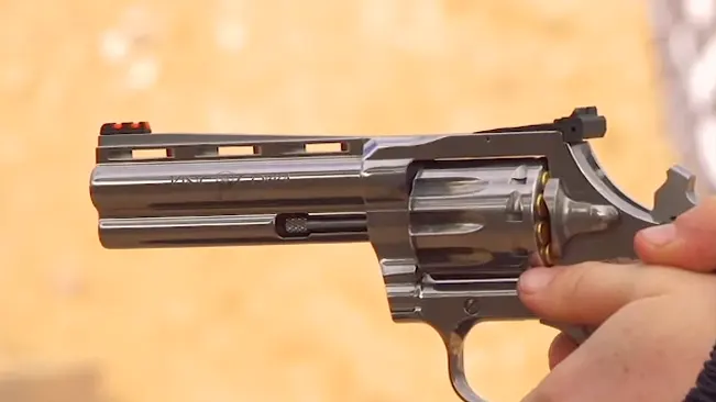 Hand holding a King Cobra Target .22 revolver with orange front sight and stainless steel finish.