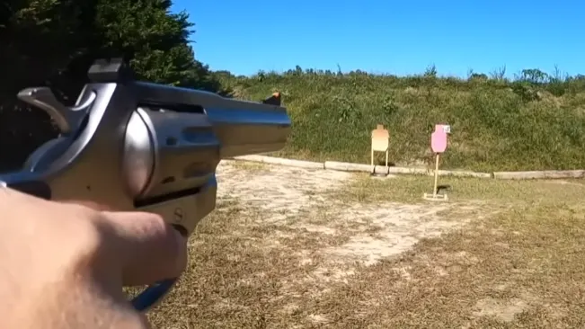 Person aiming a Rock Island Armory AL22M revolver at targets in an outdoor range.