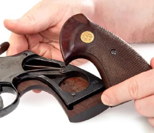 Hands replacing the checkered wooden grip on a Colt Blued Python revolver.