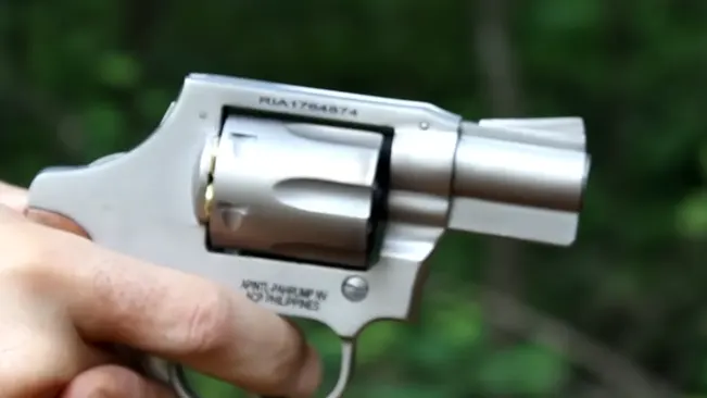 Hand holding a Rock Island M206 Spurless Matte revolver with natural background.