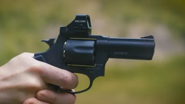 Hand holding a Taurus 856 TORO revolver with an attached Holosun red dot sight, outdoors.